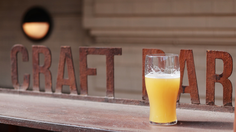 A glass filled with beer on a countertop sitting in front of a sign reading "craft bar"