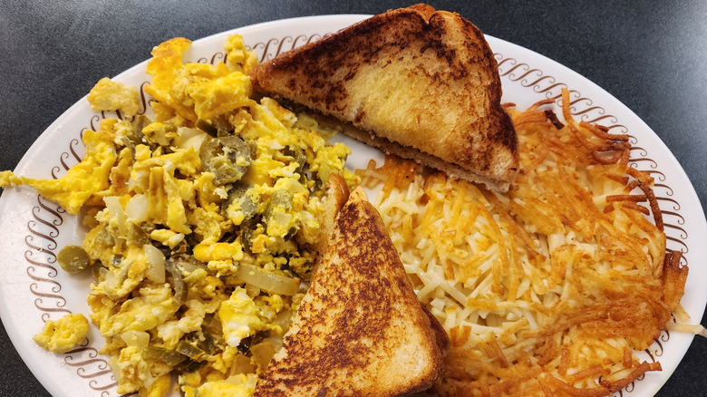 A plate of scrambled eggs with onions and jalapenos, hash browns, and toast from a Waffle House restaurant
