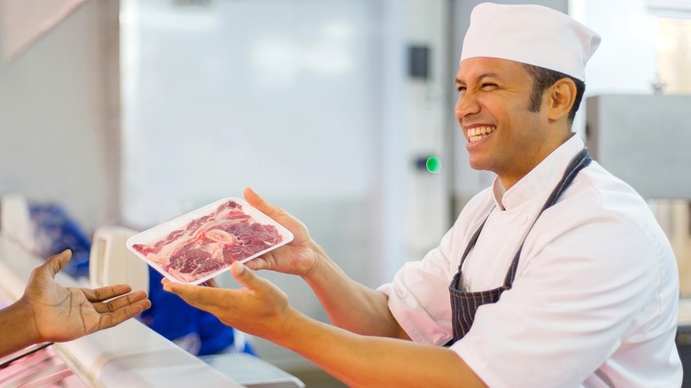 Friendly butcher handing meat package to customer.