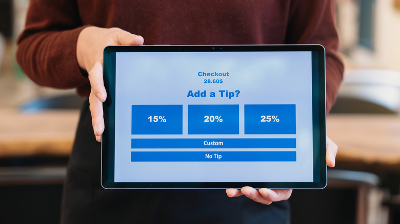 Hand holding a tablet with a screen to add a tip to a purchase.
