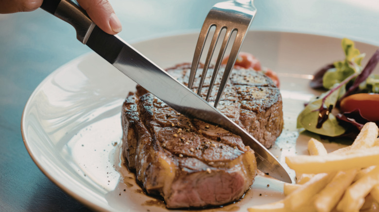 Someone cutting steak with a fork and knife at a restaurant