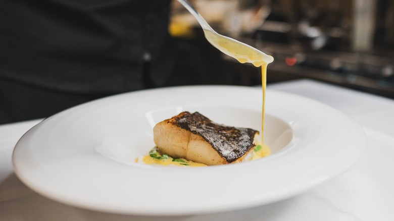 A chef drizzles sauce over a fish dish