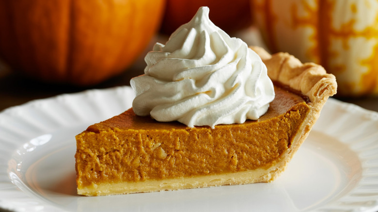 Slice of pumpkin pie topped with whipped cream on a white plate