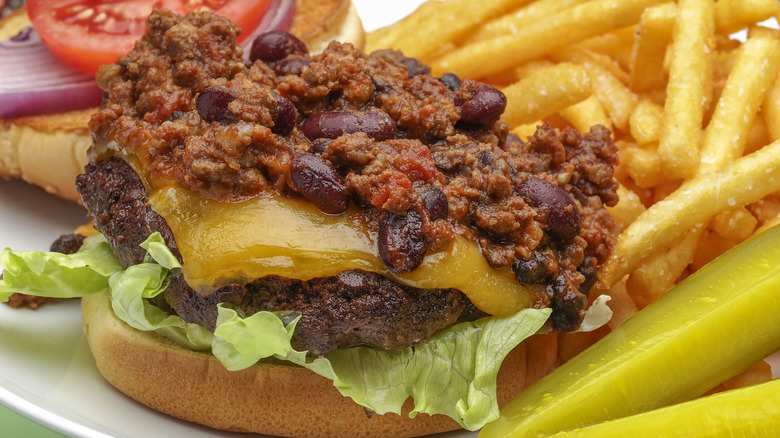 A burger patty topped with chili with fries in the background.