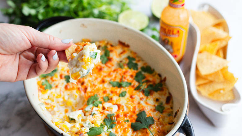 Hand lifting dip from cheesy corn dip