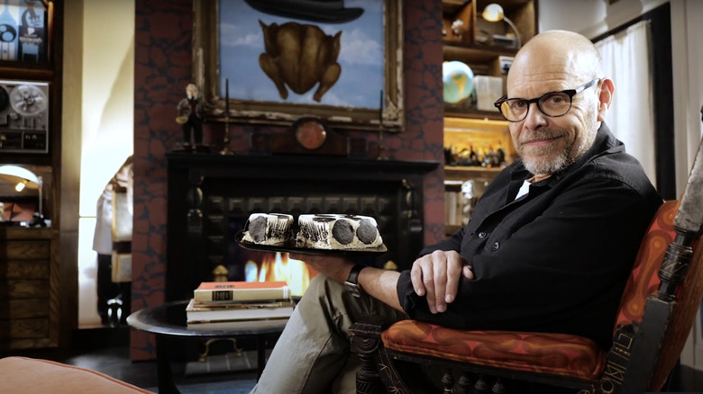 Alton Brown posing in a chair with black and white cake
