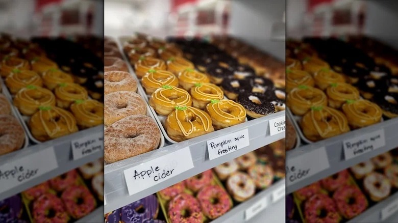 A shop cabinet of frosted donuts, including apple cider and pumpkin spice varieties.