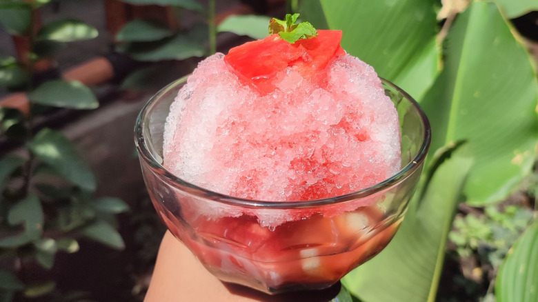 A hand holding a glass bowl of watermelon shaved ice