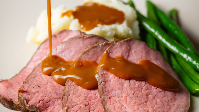 gravy sauce pouring onto roasted beef