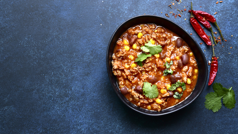 Overhead view of a bowl of meat and bean chili with dried spicy peppers on the side.