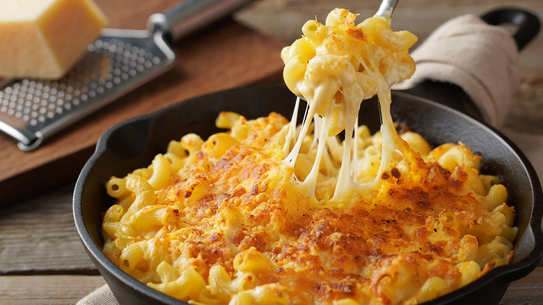 Spoon getting bite of gooey mac and cheese from a cast iron pan.