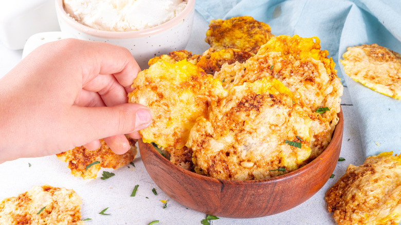 Hand grabbing a crispy cottage cheese chip from a bowl.