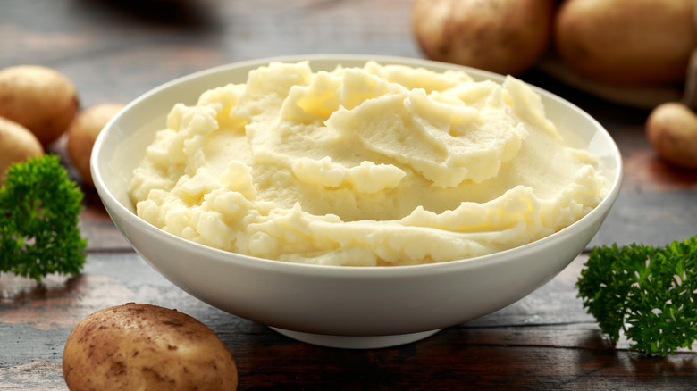 Bowl of fluffy mashed potatoes with parsley and whole potatoes surrounding it.