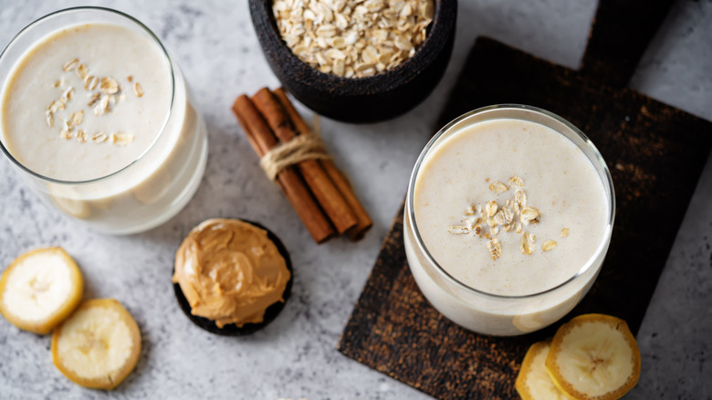 two cups of peanut butter protein shake with other ingredients on white marble surface