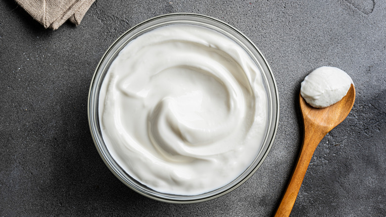 a bowl of whipped cream beside wooden spoon with cream against gray background