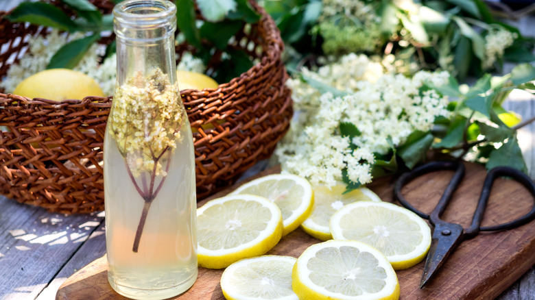 Lemon and elderflower syrup in a bottle on a cutting board with lemon slices.