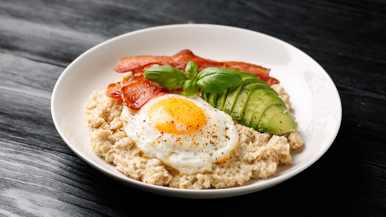 savory oatmeal with bacon, avocado, and a fried egg in a white bowl