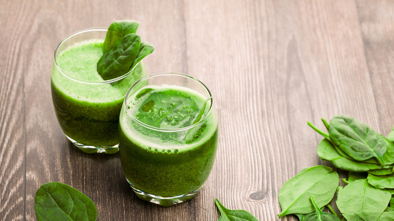 Two glasses full of green smoothie with fresh spinach leaves.