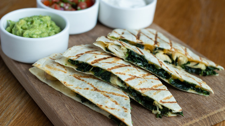 Sliced spinach and chicken quesadilla with dishes of guacamole, sour cream, and salsa.