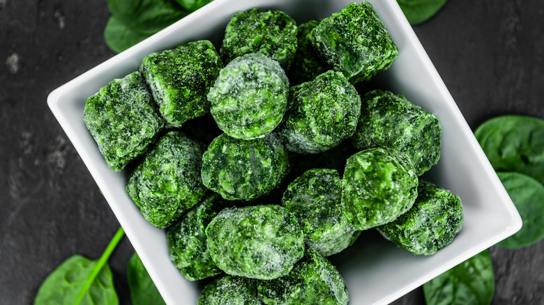 Overhead view of a white bowl full of frozen spinach cubes.