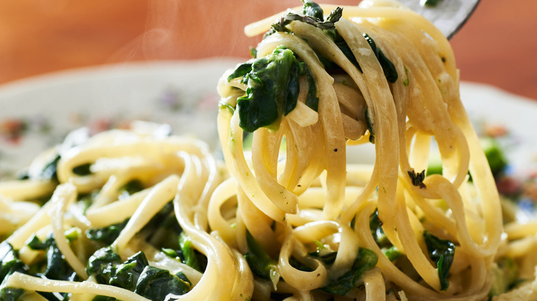 Fork grabbing linguine noodles with spinach from a plate.