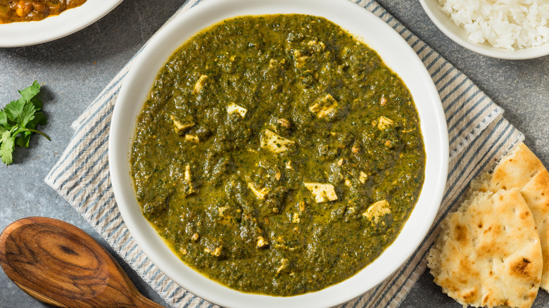 White bowl of palak paneer curry with naan on the side.
