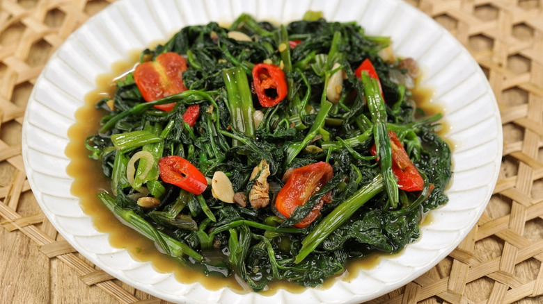 Bowl of stir-fried spinach and peppers with soy sauce and sliced nuts.