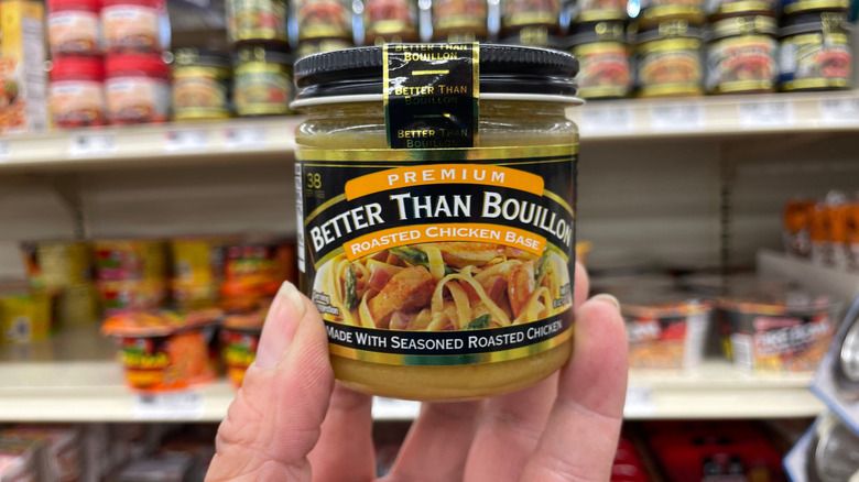 A hand holding a jar of Better Than Bouillon Roasted Chicken Base, with a shelf of similar products in the background