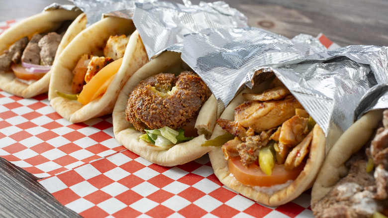 Four indulgent gyro wraps, nestled in foil and placed on a checkered paper placemat