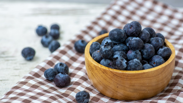 Blueberries arranged in a wooden bowl on a checkered mat