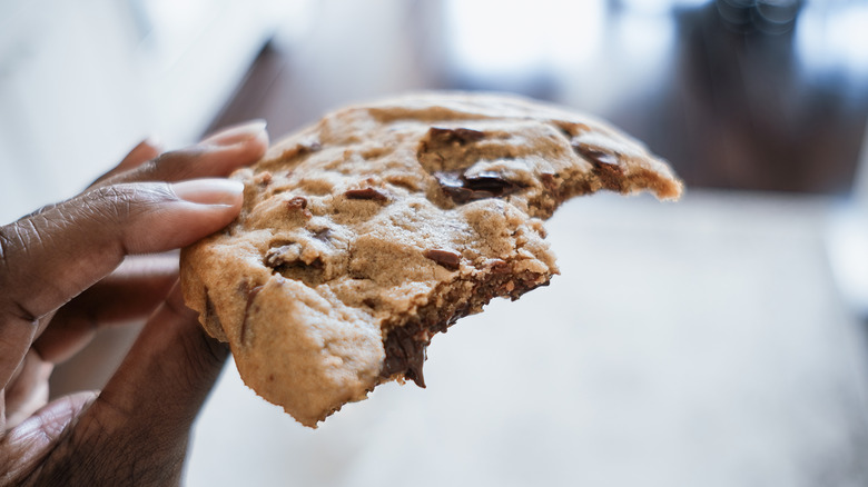 A hand holding a partially eaten cookie with gooey chocolate inside