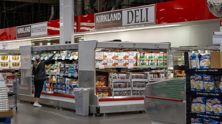 An interior shot of Costco, specifically at the rotisserie and deli section, where a person is shopping for cheese