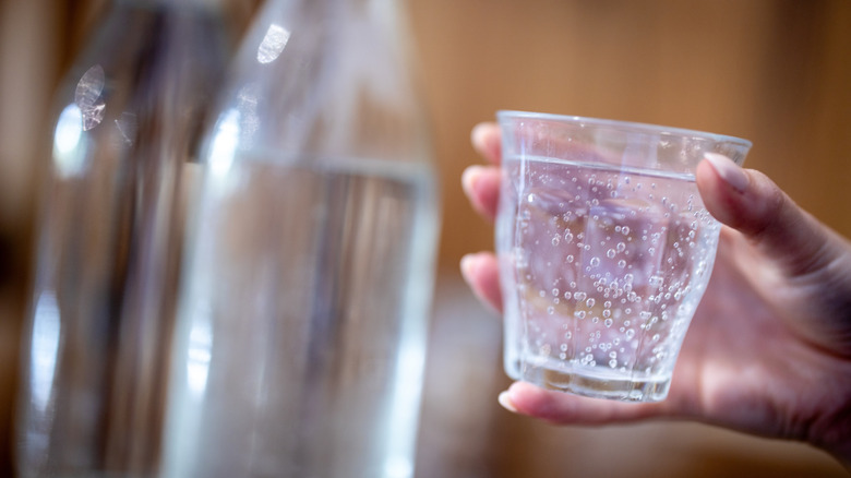 A hand holding a glass of sparkling water