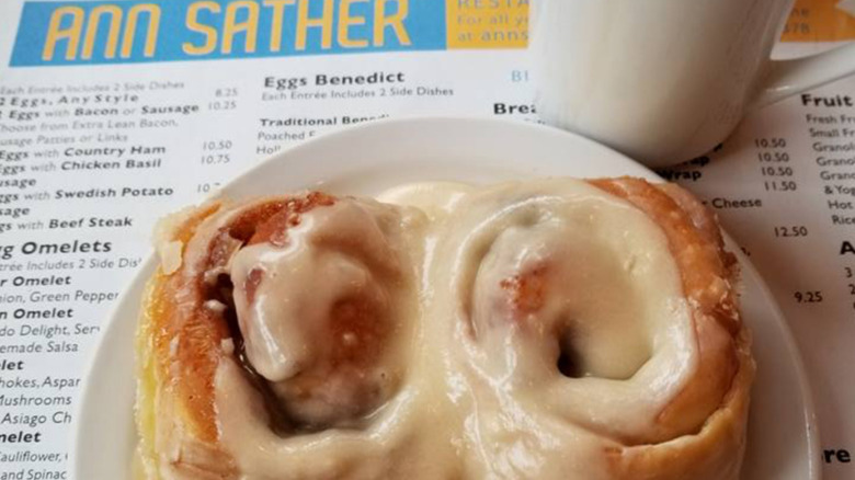 Two cinnamon rolls on a plate, with the Ann Sather menu visible in the background