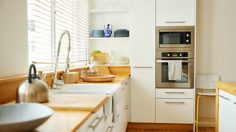 A simple, clean kitchen with white shelves and cabinets, and wooden countertops.
