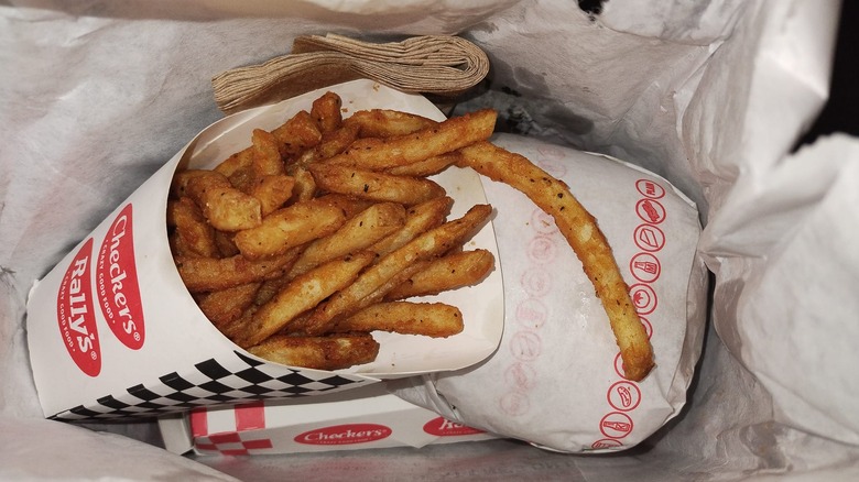 Rally's fries next to a sandwich in a fast food bag