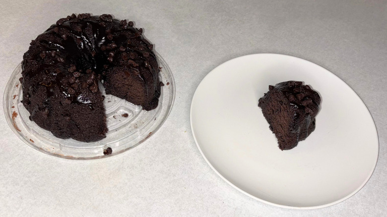 A chocolate bundt cake with chocolate chips and one slice of cake on a white plate.