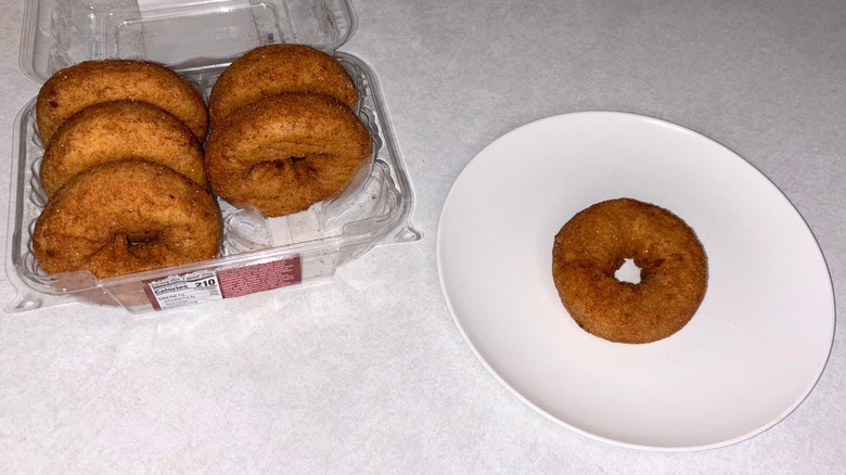 A container of apple cider donuts and one on a white plate.