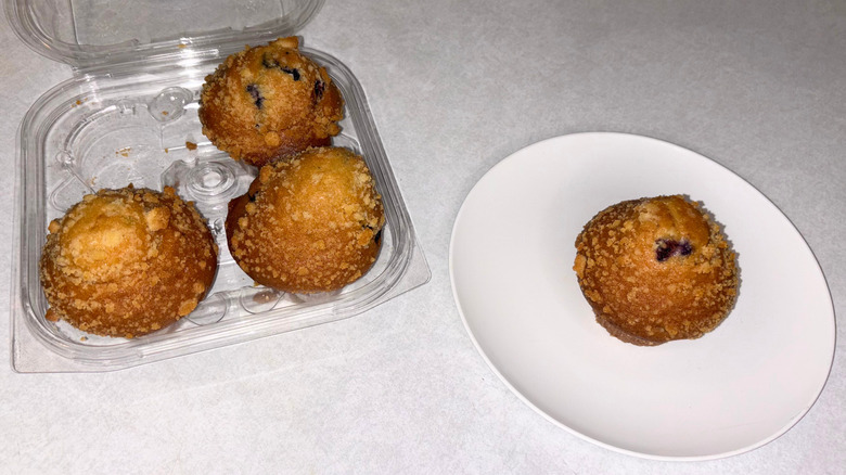 Container of blueberry muffins and one on a white plate.