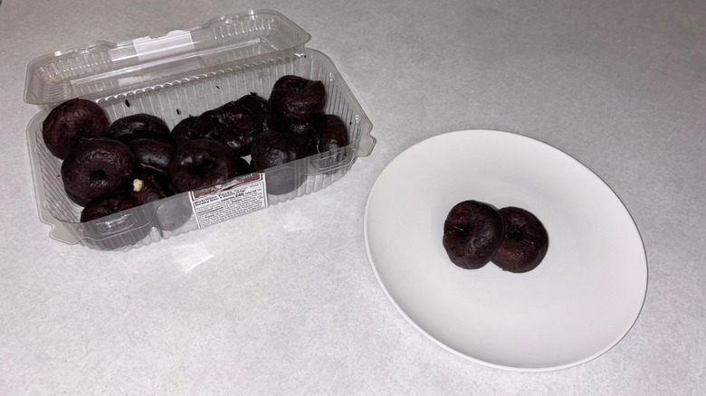 Chocolate mini donuts in a container and two donuts on a white plate.