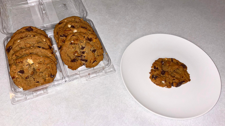 A container of kitchen sink cookies and one on a white plate.