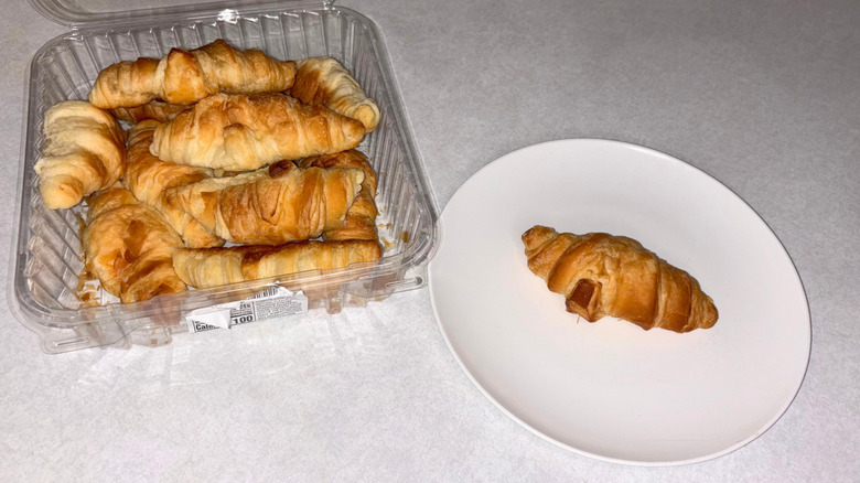 A container of mini croissants and one on a white plate.