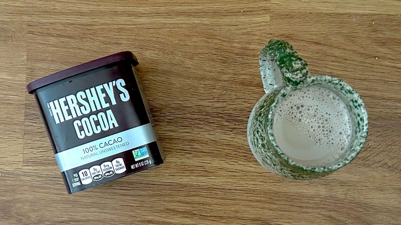 Container of Hershey's Cocoa Powder and hot chocolate in a green mug