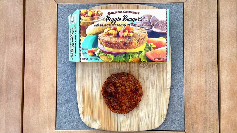 A box of Trader Joe's Cowboy Quinoa Veggie Burgers on a cutting board next to a grilled patty