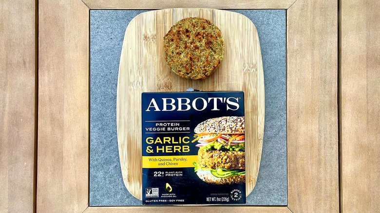 A box of Abbot's Roasted Garlic & Quinoa Veggie Burgers on a cutting board next to a grilled patty