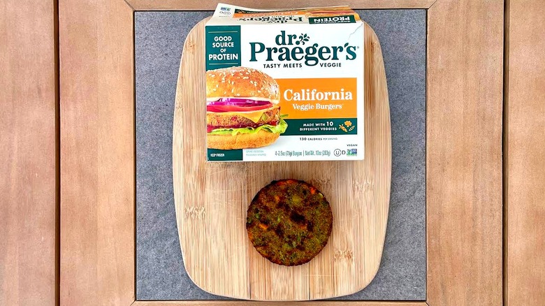 A box of Dr. Praeger's California Veggie Burgers on a cutting board next to a grilled patty