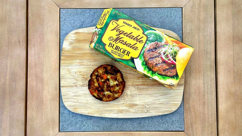 A box of Trader Joe's Vegetable Masala Burgers on a cutting board with a grilled patty
