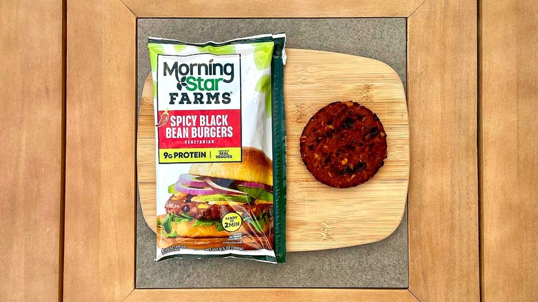 A bag of MorningStar Farms Spicy Black Bean Burgers on a cutting board next to a grilled patty