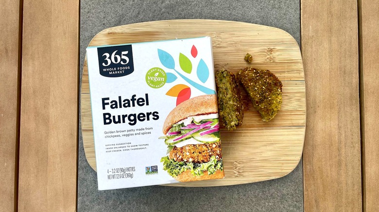 A grilled 365 by Whole Foods Market Falafel Burger on a cutting board next to its packaging