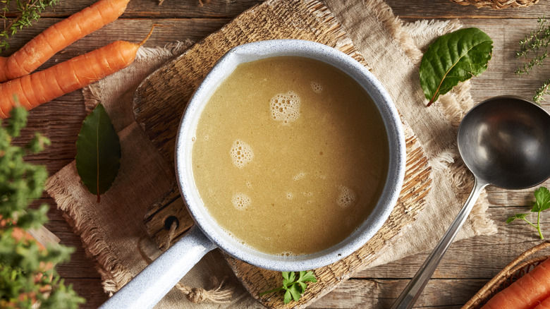 Top view of a pot of bone broth surrounded by veggies on a wooden table